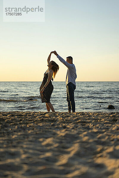Junges Paar tanzt bei Sonnenuntergang gemeinsam im Sand