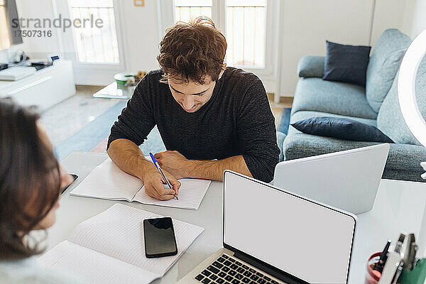 Junger Geschäftsmann schreibt in einem Buch  während er im Heimbüro arbeitet