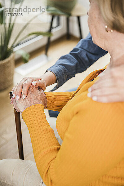 Ältere Frau und Pflegekraft stapeln zu Hause die Hände
