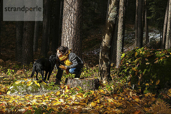 Frau in warmer Kleidung küsst Haustier im Herbstwald