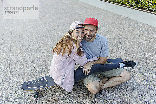 Frau umarmt Freund  der auf Skateboard am Fußweg sitzt