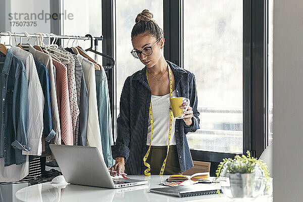 Modedesigner mit Kaffeetasse und Laptop im Büro