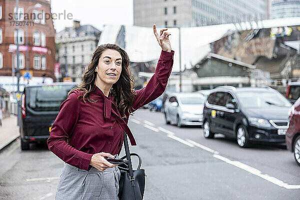 Geschäftsfrau mit erhobener Hand und rufendes Taxi auf der Stadtstraße