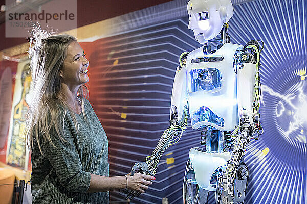 Glücklicher Techniker schüttelt in der Werkstatt einem menschlichen Roboter die Hand