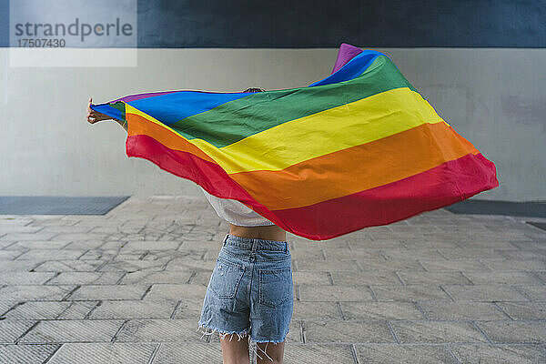 Frau mit Jeansshorts hält Regenbogenfahne auf Fußweg