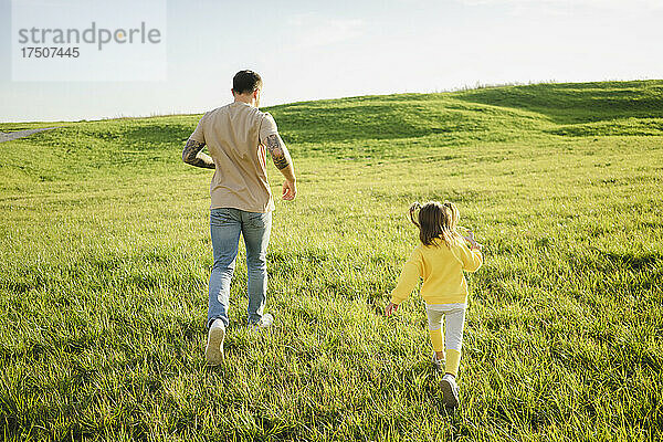 Vater und Tochter laufen auf einer Wiesenlandschaft