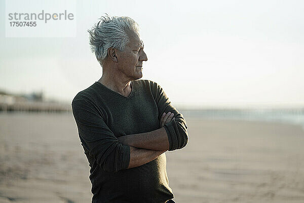 Älterer Mann mit verschränkten Armen am Strand