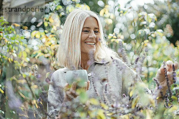 Lächelnde Frau hält Tasse im Hinterhof