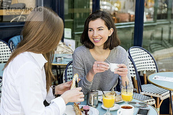Junge Frau unterhält sich mit einer Freundin und bestreicht Baguette im Café mit Butter