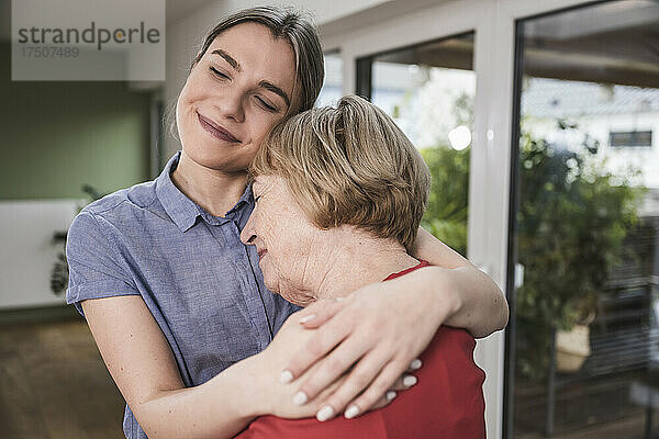 Lächelnde Pflegekraft umarmt ältere Frau zu Hause