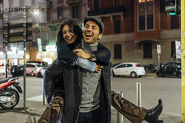 Fröhlicher Freund trägt Freundin huckepack  während er durch die Stadt geht