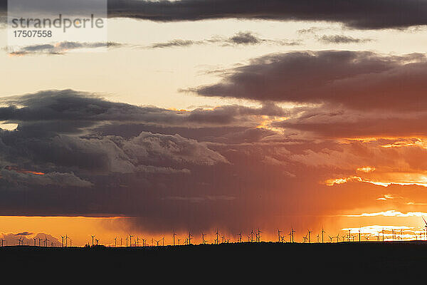 Dramatischer Sonnenuntergang über den Silhouetten entfernter Windkraftanlagen