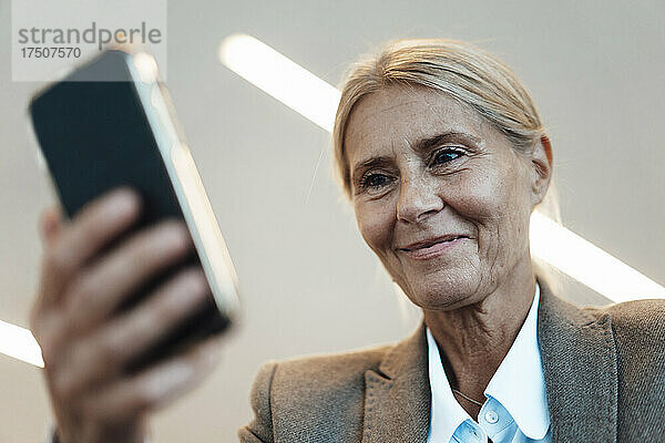 Lächelnde Geschäftsfrau benutzt Smartphone im Büro