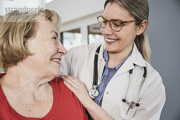 Lächelnder Arzt mit der Hand auf der Schulter des älteren Patienten zu Hause