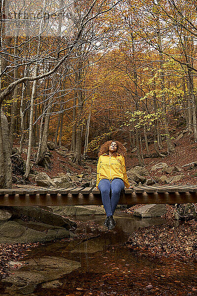 Frau entspannt sich auf Holzbrücke im Herbstwald