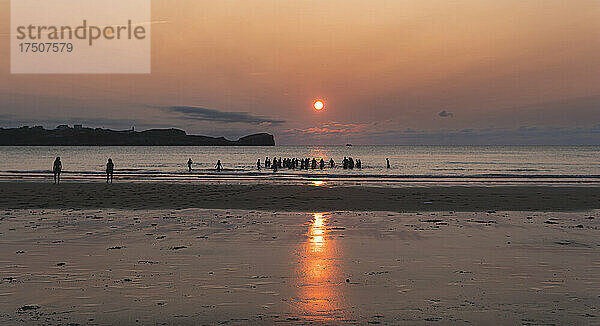 Sonnenuntergang über Silhouetten von Menschen  die sich am Küstenstrand entspannen