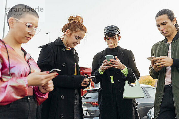 Freunde tragen Jacke und benutzen Mobiltelefone auf dem Parkplatz