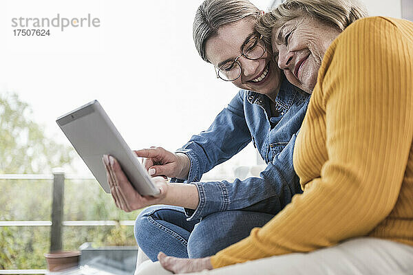 Lächelnde Pflegekraft nutzt Tablet-PC mit älterer Frau zu Hause