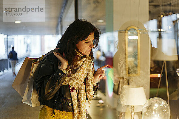 Frau mit Einkaufstüten beim Schaufensterbummel im Laden für elektrische Lampen