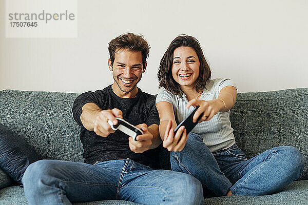 Fröhliches junges Paar spielt Videospiel auf dem Sofa im Wohnzimmer