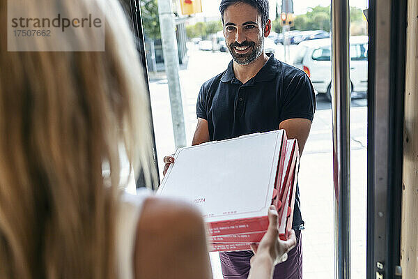 Lächelnder Lieferbote gibt Geschäftsfrau am Eingang Pizzakartons