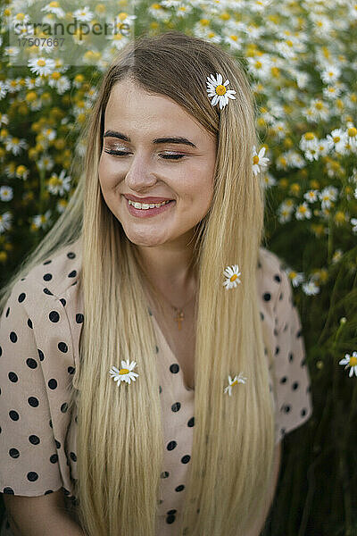 Glückliche Frau mit geschlossenen Augen und Blumen auf langen blonden Haaren