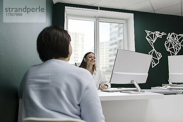 Kunde und Reisebüro diskutieren am Schreibtisch im Büro