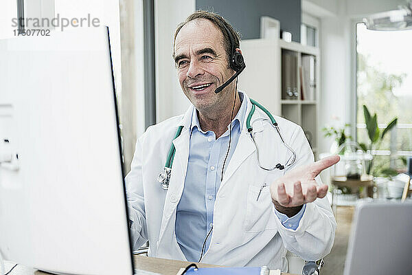Lächelnder Arzt gestikuliert bei Videoanruf in der Klinik