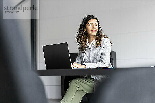 Junge Geschäftsfrau mit Laptop lächelt am Schreibtisch