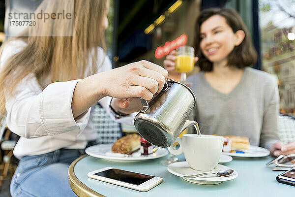 Junge Frau gießt einer Freundin im Café Kaffee in eine Tasse
