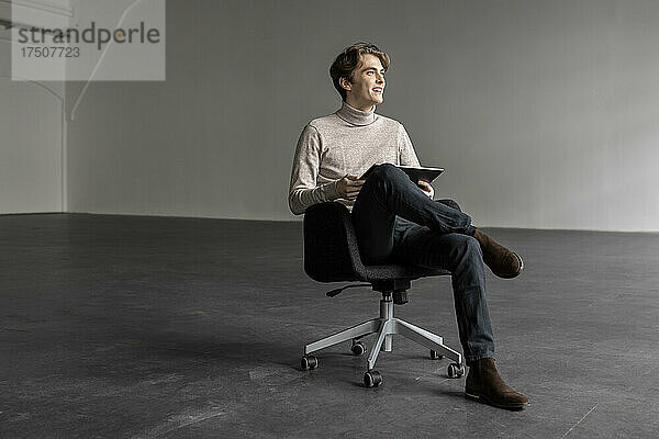 Junger Geschäftsmann mit Tablet-PC lächelt auf Stuhl in Industriehalle