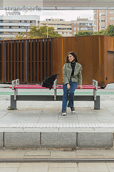 Frau mit Rucksack sitzt auf der Bank der Straßenbahnhaltestelle