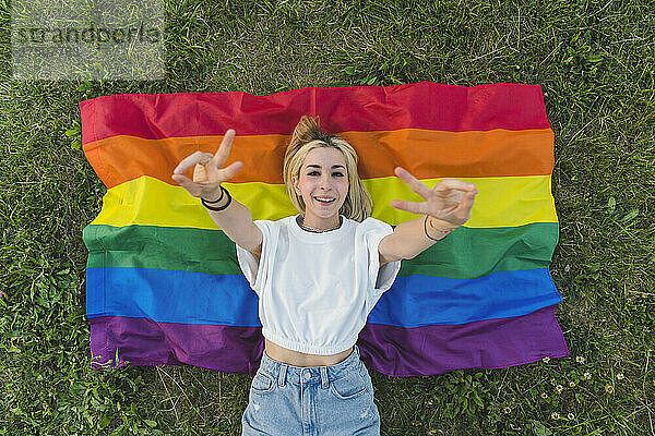 Junge Frau gestikuliert Friedenszeichen auf mehrfarbiger Flagge