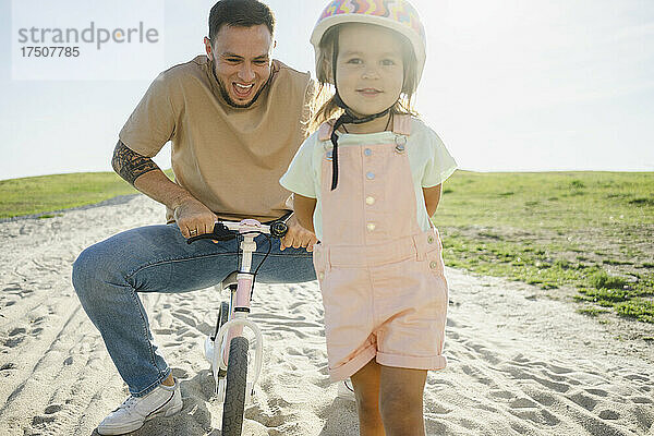 Mädchen mit Helm  im Hintergrund sitzt der Vater auf dem Fahrrad