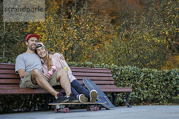 Mann mit Arm um Freundin sitzt zusammen auf Bank neben Pflanzen