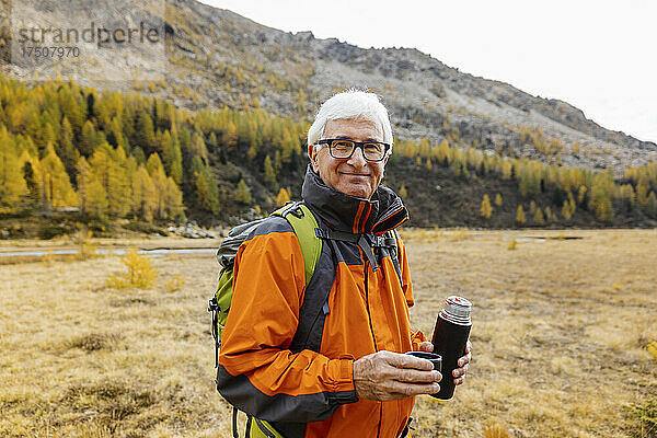 Lächelnder älterer Wanderer mit isoliertem Getränkebehälter in den Rätischen Alpen  Italien