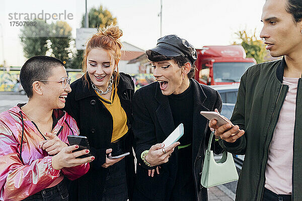 Fröhliche Freunde zeigen einander ihr Smartphone auf dem Fußweg