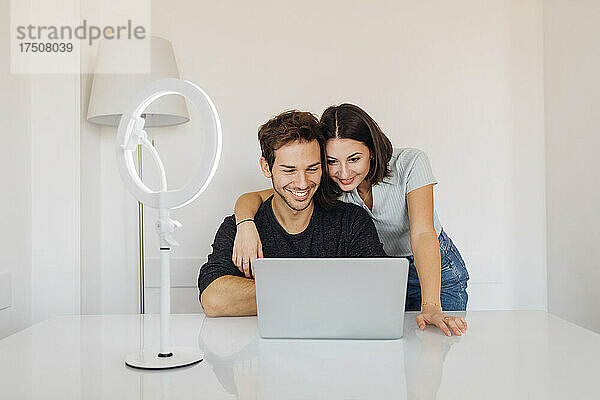 Lächelndes junges Paar  das zu Hause gemeinsam einen Laptop am Tisch benutzt