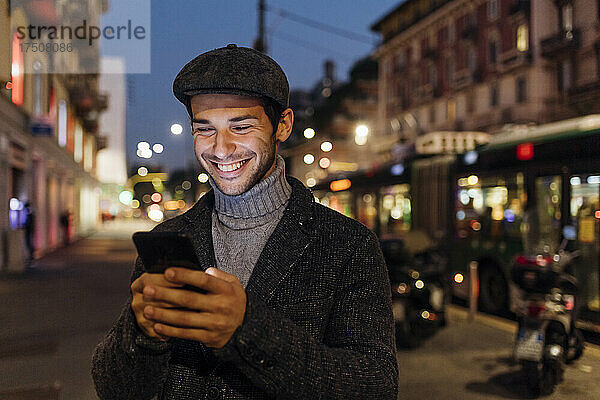 Glücklicher junger Mann  der sein Smartphone in der Stadt benutzt