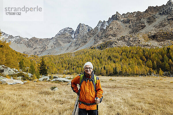 Lächelnder Tourist mit Wanderstöcken inmitten von Gras in den Rhätischen Alpen  Italien