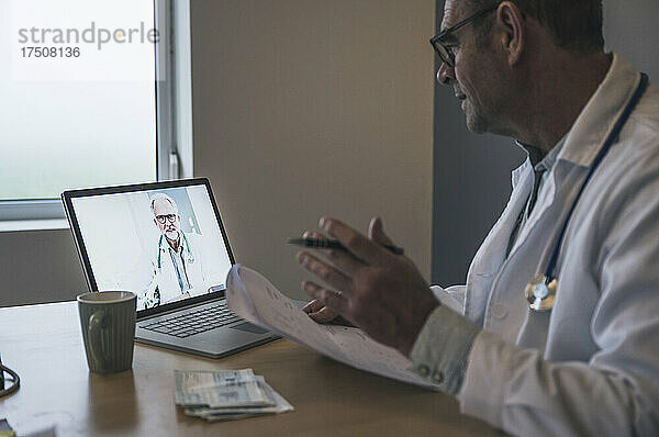 Arzt gestikuliert bei Videoanruf über Laptop mit Kollege in der Klinik