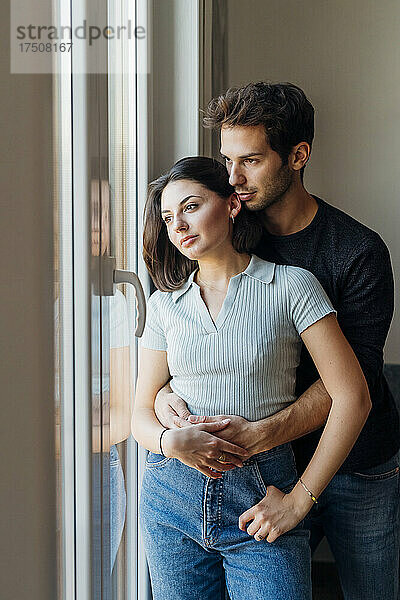 Junges Paar schaut zu Hause durch das Fenster