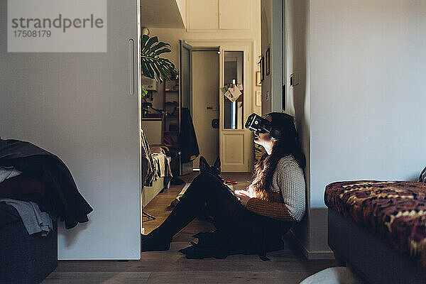 Frau mit Virtual-Reality-Headset sitzt zu Hause an der Wand
