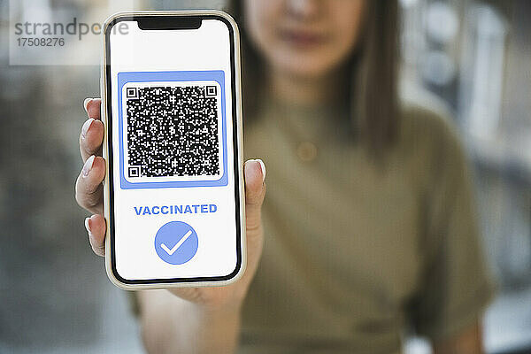 Frau zeigt geimpften QR-Code mit Häkchensymbol auf dem mobilen Bildschirm