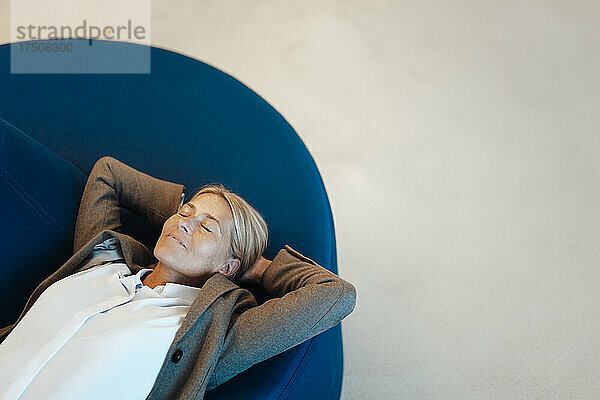 Geschäftsfrau mit den Händen hinter dem Kopf und geschlossenen Augen entspannt sich im Büro