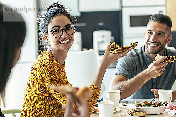 Lächelnde Kollegen mit Pizza und Blick auf die Geschäftsfrau im Büro