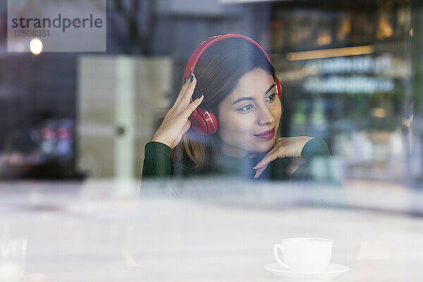 Frau hört Musik über Kopfhörer am Caféfenster