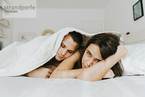 Mann stützt sich im Schlafzimmer auf Frau unter Bettdecke