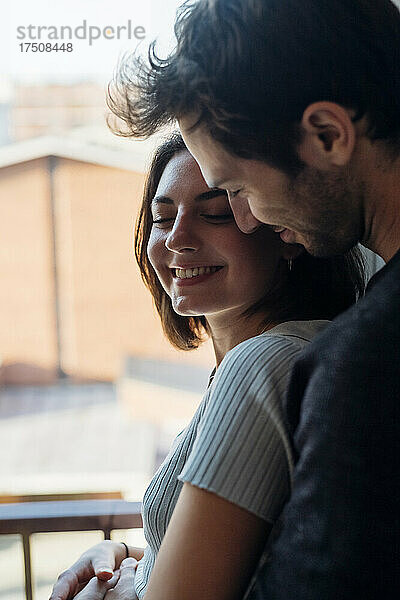 Lächelndes junges Paar  das zu Hause am Fenster steht