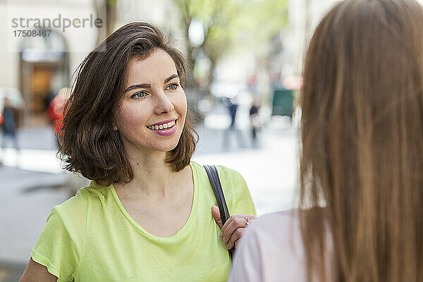 Schöne junge Frau mit kurzen Haaren im Gespräch mit einer Freundin auf dem Fußweg